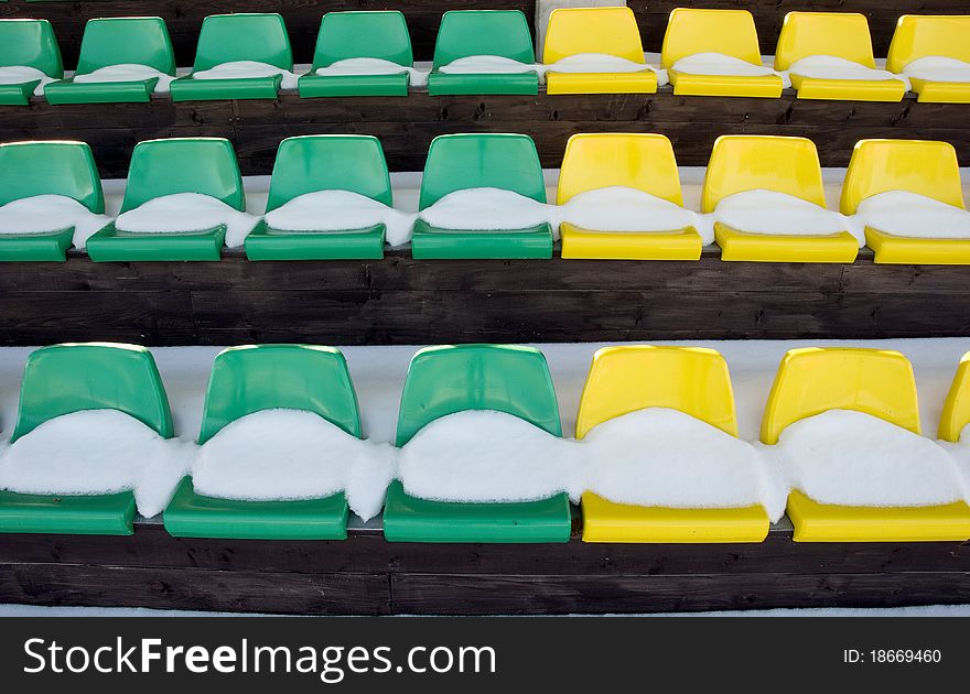 Football stadium tribune yelow and green chairs with winter snow