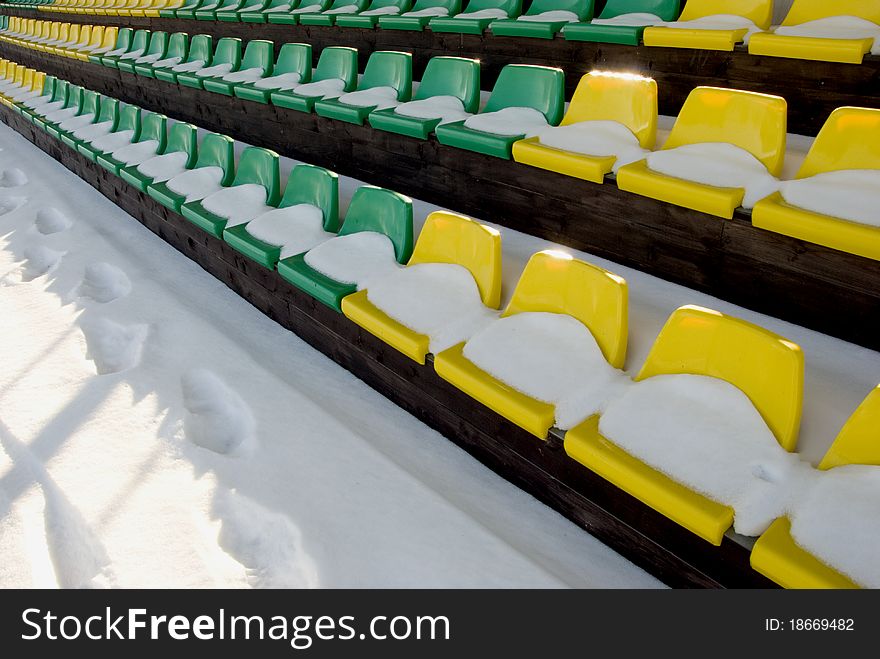 Football stadium tribune yelow and green chairs with winter snow