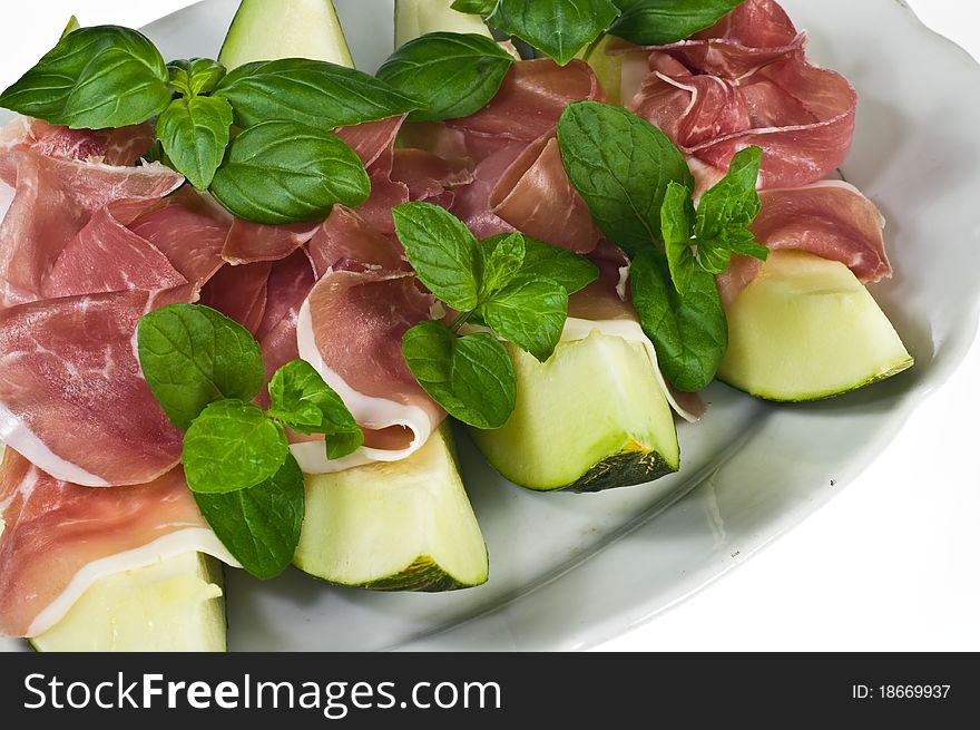 Melon with italian ham and basil leaves on porcelain dish. Melon with italian ham and basil leaves on porcelain dish