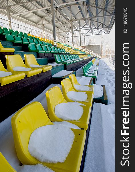 Football stadium tribune yelow and green chairs with winter snow