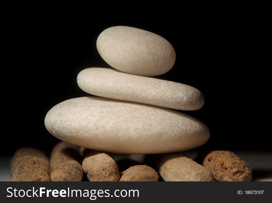 Three stones balancing on each other on drift wood and black backdrop. Three stones balancing on each other on drift wood and black backdrop