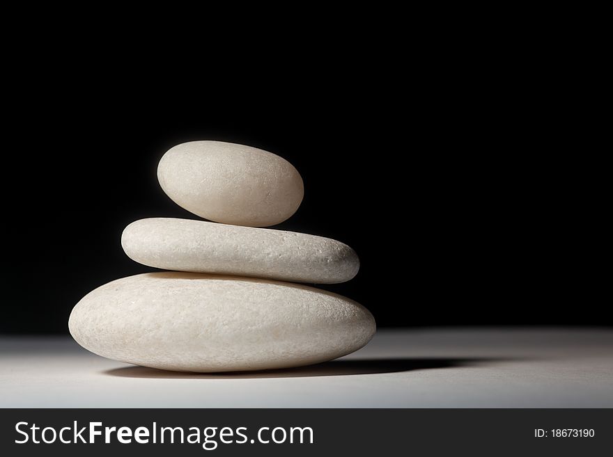 Three stones balancing on each other on a white sheet and black backdrop. Three stones balancing on each other on a white sheet and black backdrop