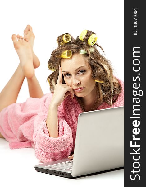 Young adult girl in pink dressing gown and with hair rollers lying with laptop. Young adult girl in pink dressing gown and with hair rollers lying with laptop