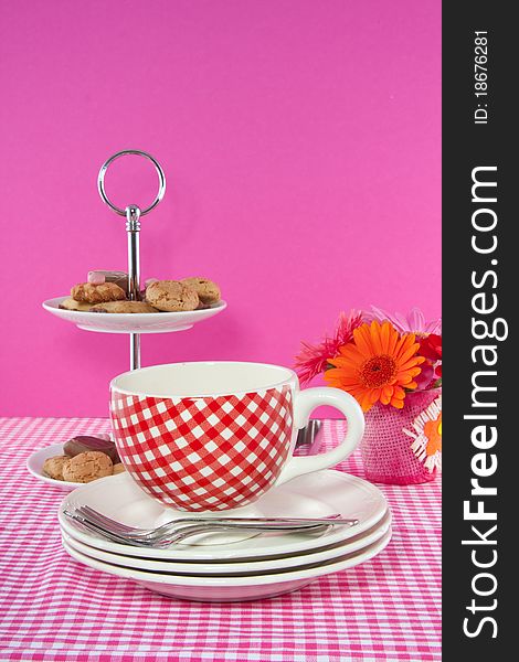 A cup and saucer on a checkered tablecloth and a serving bowl with cookies and chocolate. A cup and saucer on a checkered tablecloth and a serving bowl with cookies and chocolate