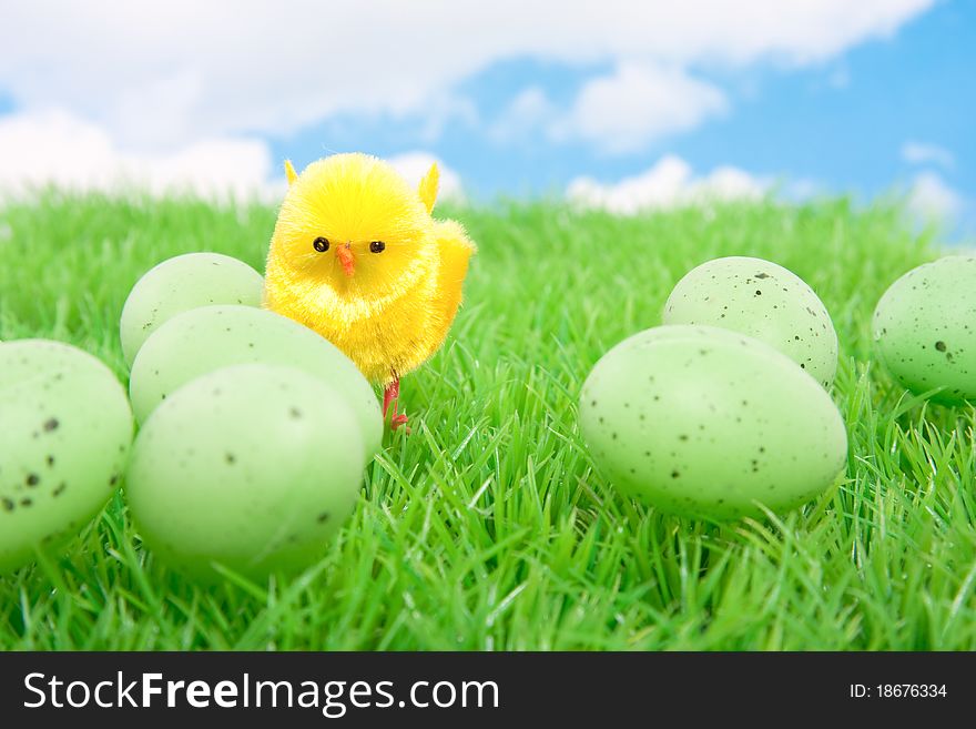 A yellow chick with easter eggs on a green lawn against a cloudy sky