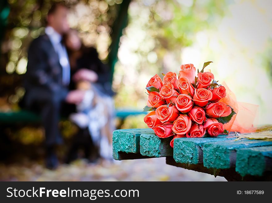 Bridal bouquet of red roses on a green meadow and blurred newlyweds. Bridal bouquet of red roses on a green meadow and blurred newlyweds