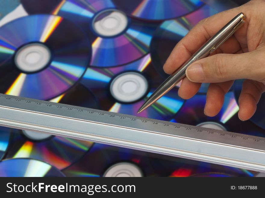 A hand holding a pen near a ruler against a background of discs. A hand holding a pen near a ruler against a background of discs.