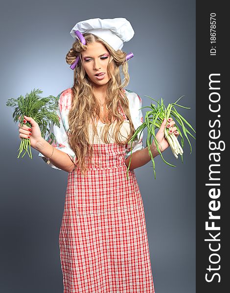 Beautiful blonde woman housewife holding greens. Studio shot over grey background.