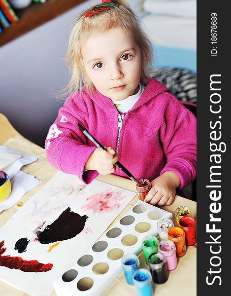 Beautiful little girl is drawing with gouaches on paper