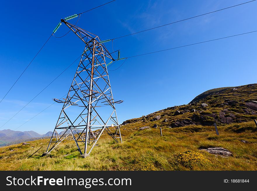 Electric power pole in mountains under blue sky.