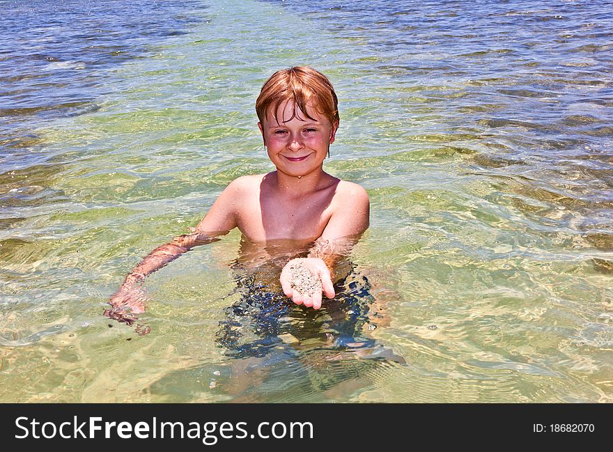 Boy has fun in the clear atlantic ocean and holds a shell with sand in the hand. Boy has fun in the clear atlantic ocean and holds a shell with sand in the hand