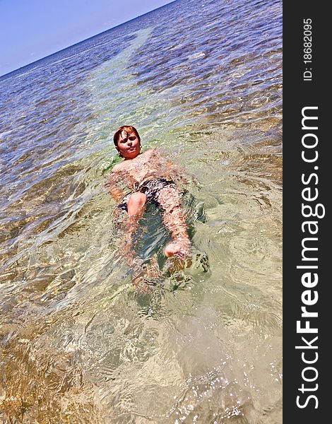 Boy swims on his back in the beautiful clear ocean