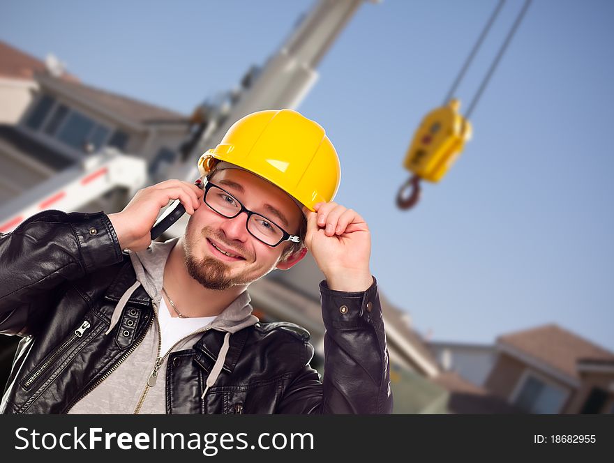Young Contractor Wearing Hard Hat on Cell Phone In Front of Utility Crane. Young Contractor Wearing Hard Hat on Cell Phone In Front of Utility Crane.