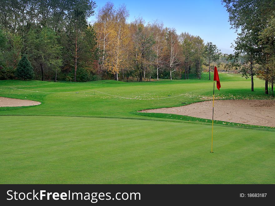 Golf meadow and autumnal forest. Red flag.