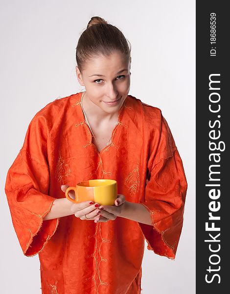 Girl in orange dress on a light background with a cup. Girl in orange dress on a light background with a cup