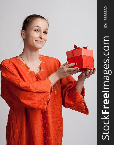Smiling girl in orange dress on a light background with a gift in the hands of. Smiling girl in orange dress on a light background with a gift in the hands of