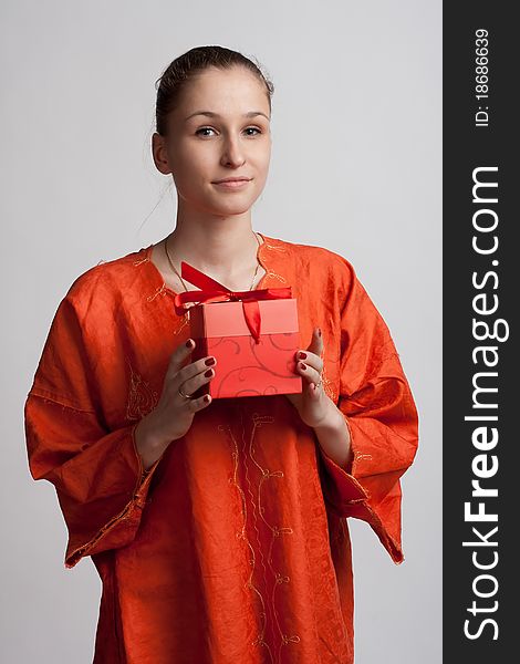 Girl in orange dress on a light background with a gift in the hands of. Girl in orange dress on a light background with a gift in the hands of