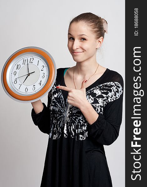 Beautiful girl on a white background shows the finger at the large clock in his hand which is almost noon. Beautiful girl on a white background shows the finger at the large clock in his hand which is almost noon