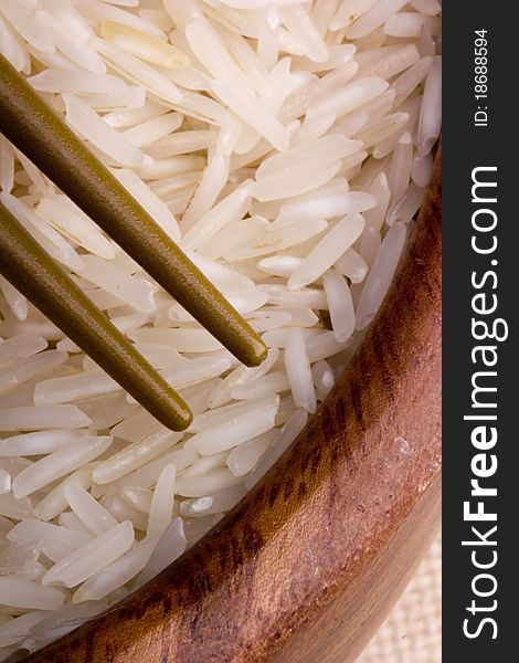 Close-up of white rice in a brown plate and golden chopsticks.