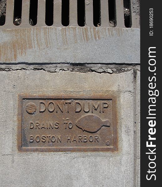 A metal sign cemented in concrete on Boston MA USA sidewalk next to storm drain. An environmental reminder to keep the harbor clean. A metal sign cemented in concrete on Boston MA USA sidewalk next to storm drain. An environmental reminder to keep the harbor clean