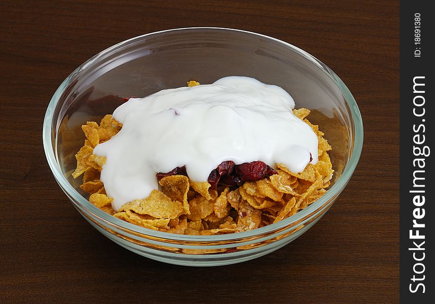 Cornflakes with dried cranberries and yogurt in glass bowl on dark wooden table