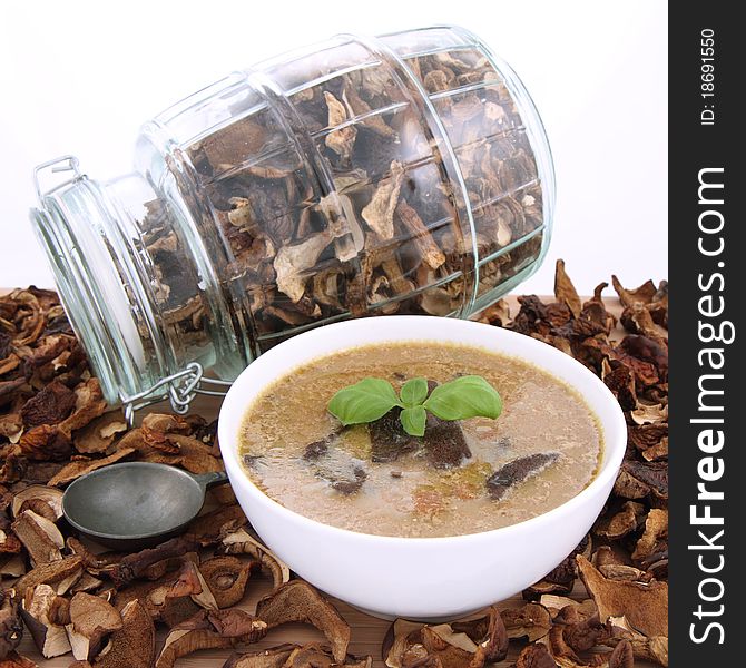 Mushroom soup in a bowl, decorated with basil, with dried mushrooms surrounding it and some in a jar, and an antique spoon. Mushroom soup in a bowl, decorated with basil, with dried mushrooms surrounding it and some in a jar, and an antique spoon