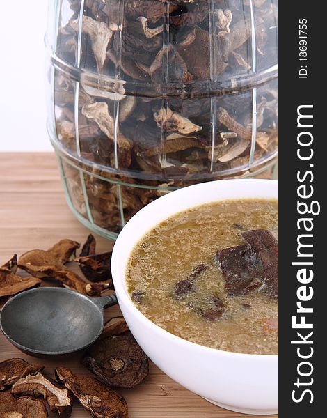 Mushroom soup in a bowl with dried mushrooms surrounding it and some in a jar, and an antique spoon