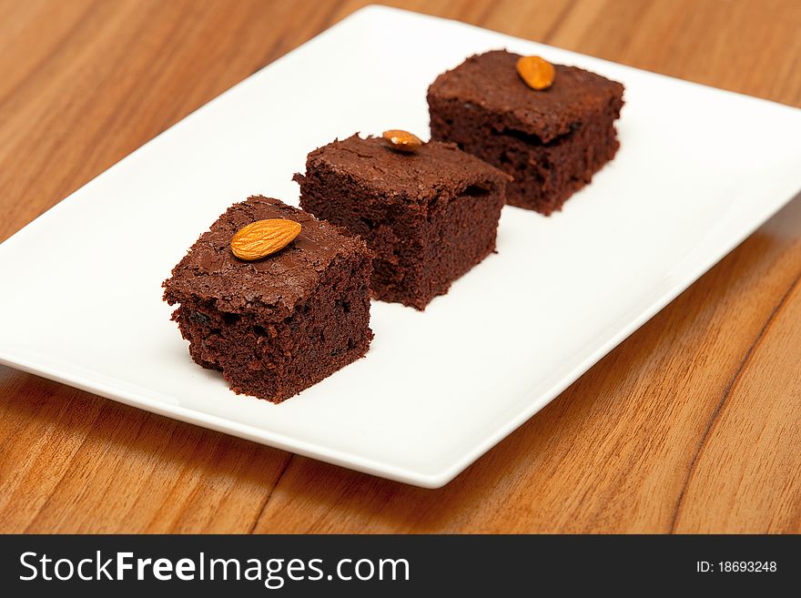 Three brownies with almonds on a white plate and wooden background