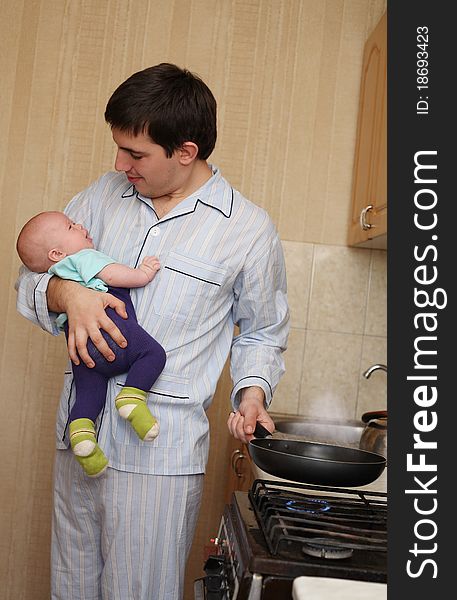 The young father with the baby on hands cooks food. The young father with the baby on hands cooks food