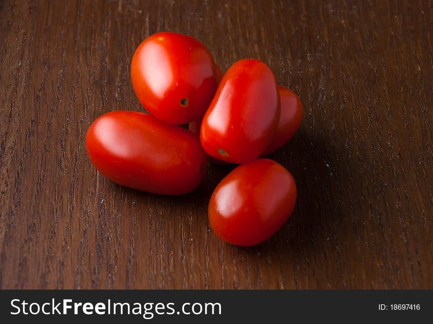 Five red cherry tomatoes stacked on a wood table. Five red cherry tomatoes stacked on a wood table.
