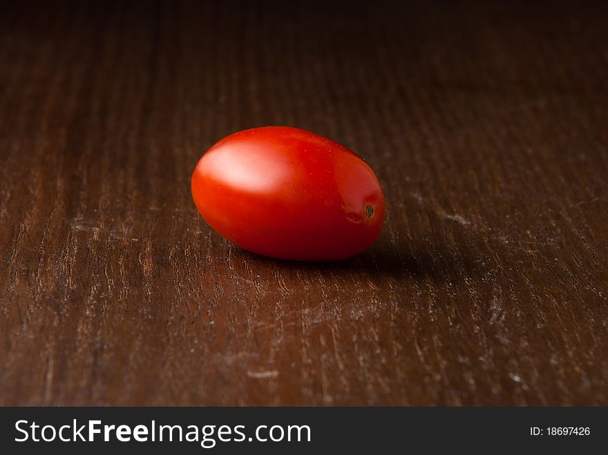 One single red cherry tomato on a wood table. One single red cherry tomato on a wood table