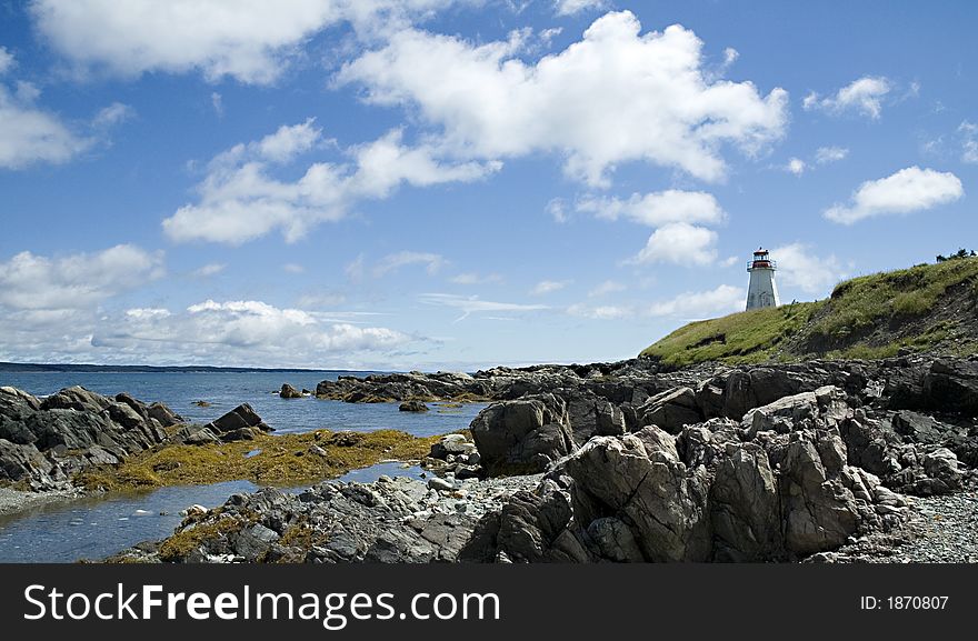 Lighthouse overlooking a rocky shore and cloud studded sky. Lighthouse overlooking a rocky shore and cloud studded sky.