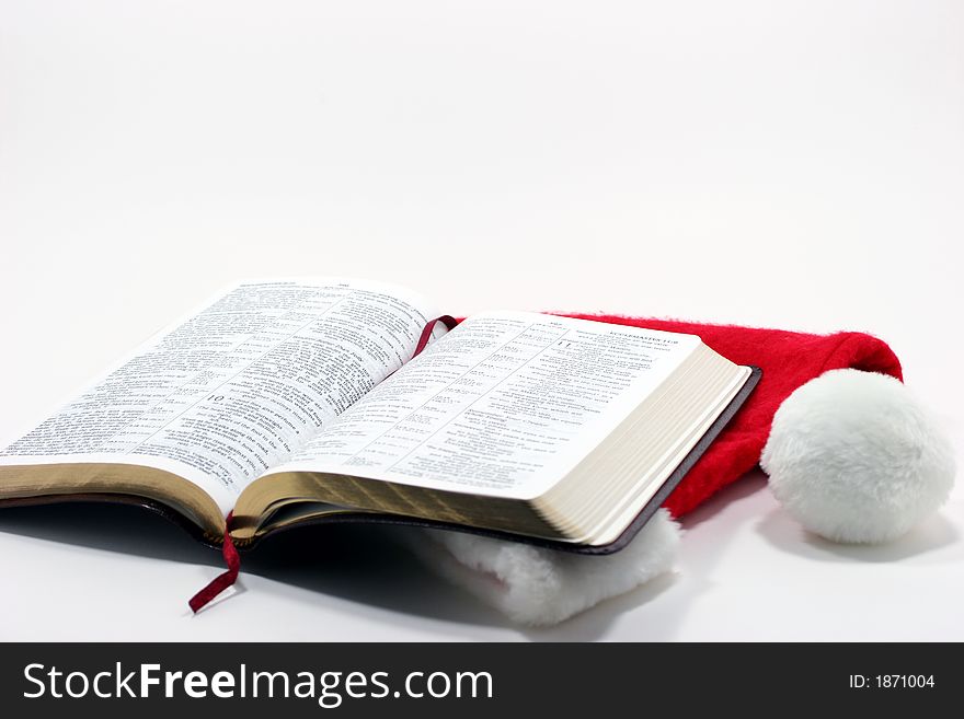 Open Bible on top of a Santa hat isolated on a white background. Open Bible on top of a Santa hat isolated on a white background.