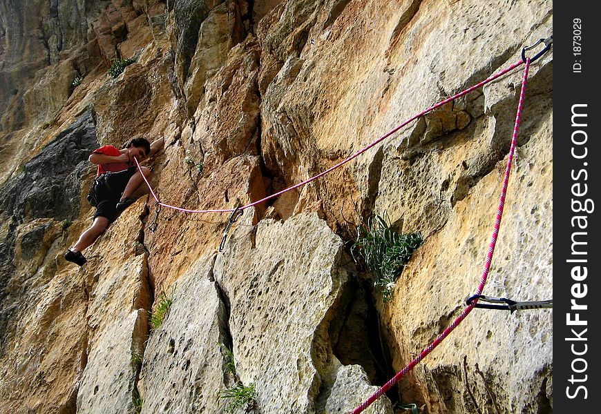 A young man is helping his teeth to delay a roap when he's climbing on a rock. A young man is helping his teeth to delay a roap when he's climbing on a rock