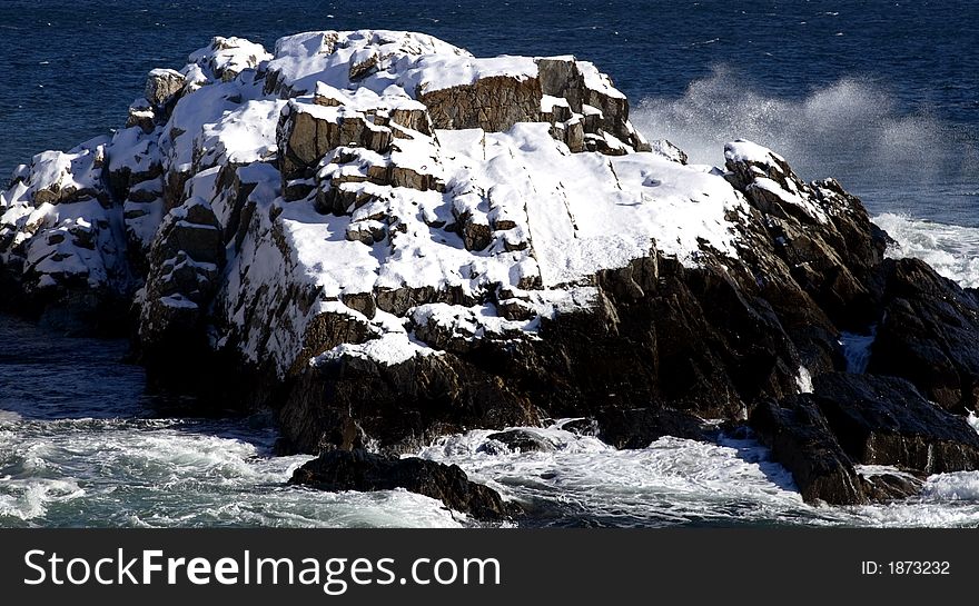 Snow covered rocks in the ocean with waves crashing