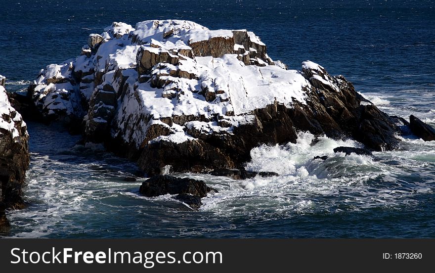 Snow covered rocks in the ocean with waves crashing