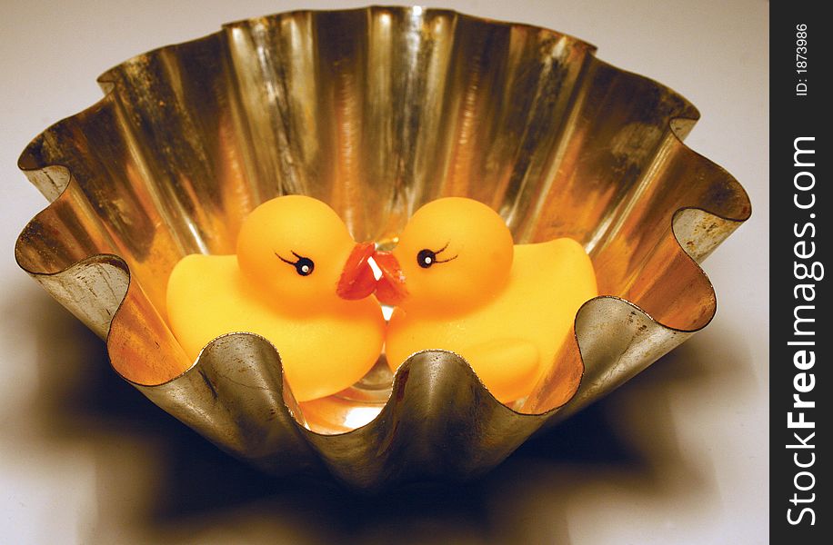 A pair of rubber ducks kissing in a metal cup. A pair of rubber ducks kissing in a metal cup