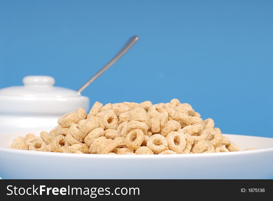 Oat cereal in white bowl with sugar bowl on blue background