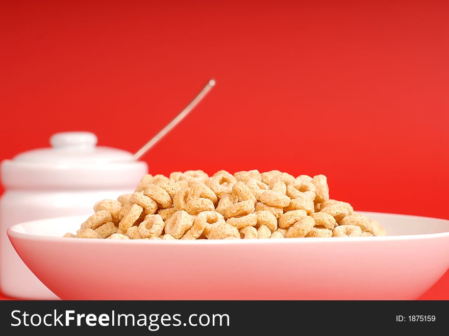 A bowl of oat cereal with sugar bowl on red background