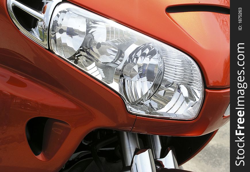 Close-up detail of a motorcycle headlamp, showing part of the fairing and the off-side headlamp and light cluster. Close-up detail of a motorcycle headlamp, showing part of the fairing and the off-side headlamp and light cluster