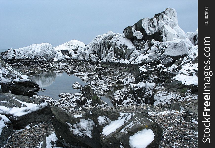 Snow-covered rocks at low tide, and a small tidal pool on the shore of the Atlantic ocean