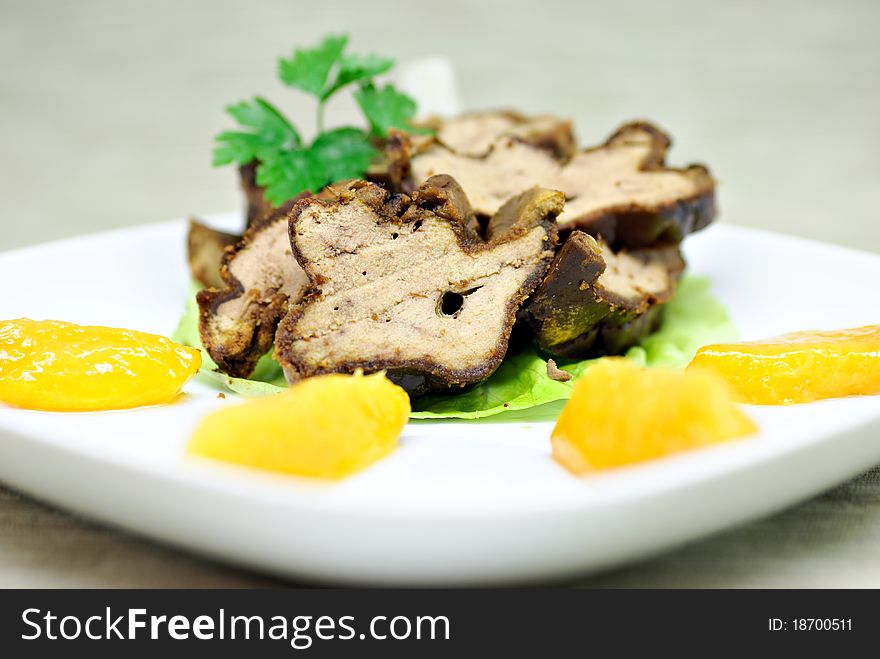 Roasted duck liver with peach on white plate.