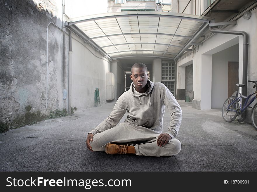 Young african man sitting on a street in front of a block of flats. Young african man sitting on a street in front of a block of flats