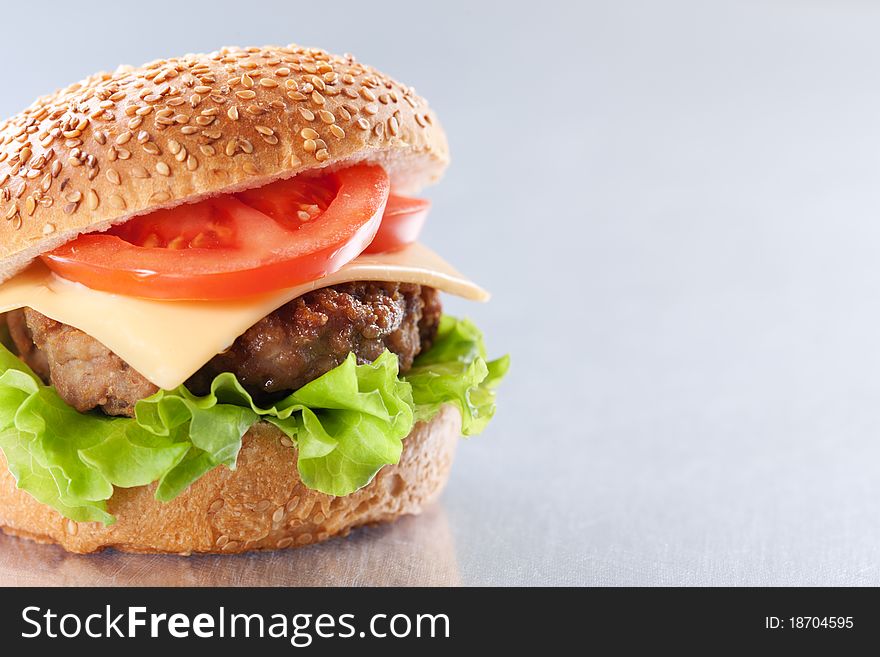 Cheeseburger with tomatoes and lettuce on grey background