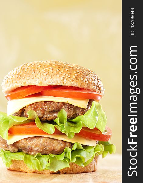 Double cheeseburger with tomatoes and lettuce on yellow background