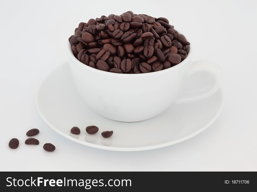 Coffee beans in a porcelain cup with saucer and scattered, over white background. Coffee beans in a porcelain cup with saucer and scattered, over white background.