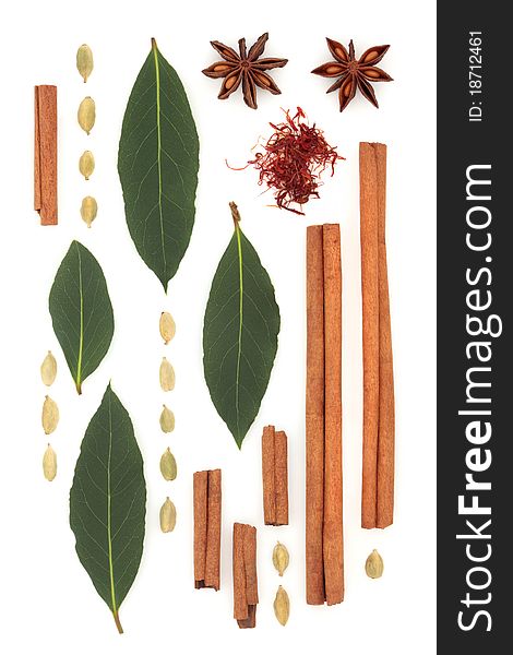 Spice and herb abstract design of saffron, cinnamon sticks, star anise, bay leaf and cardamom pods, over white background.