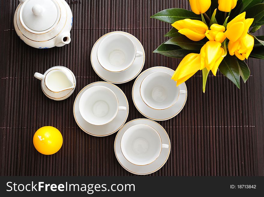 Tea set on a bamboo mat with yellow tulips and yellow candle in the form of eggs. Tea set on a bamboo mat with yellow tulips and yellow candle in the form of eggs