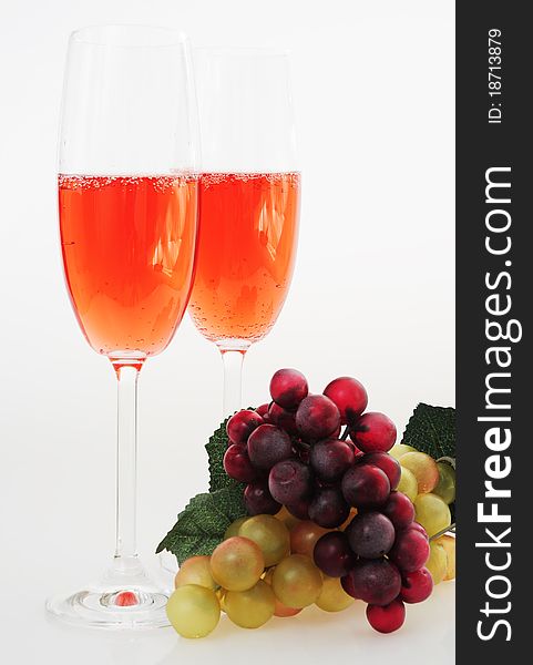 Two glasses of pink champagne on a white background, a branch of white and black grapes