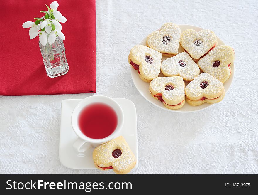 Fruit tea in a white cup cakes in the shape of hearts, red napkin and snowdrops. Fruit tea in a white cup cakes in the shape of hearts, red napkin and snowdrops